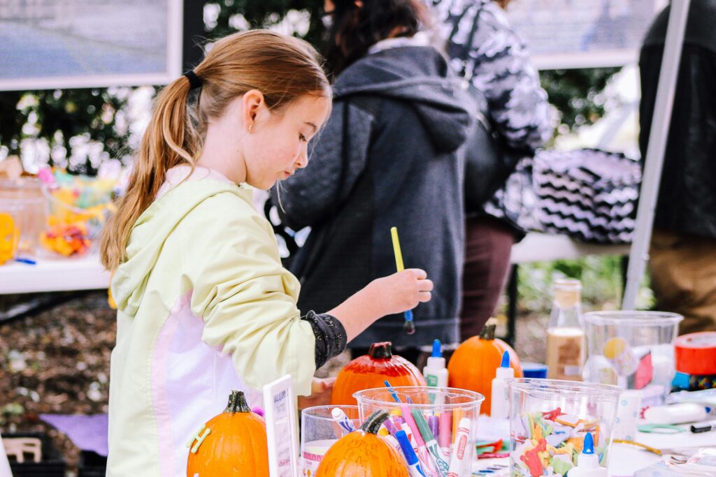 pexels-photo-1518836-1518836 A child enjoys painting pumpkins at an outdoor crafting event, surrounded by art supplies.
